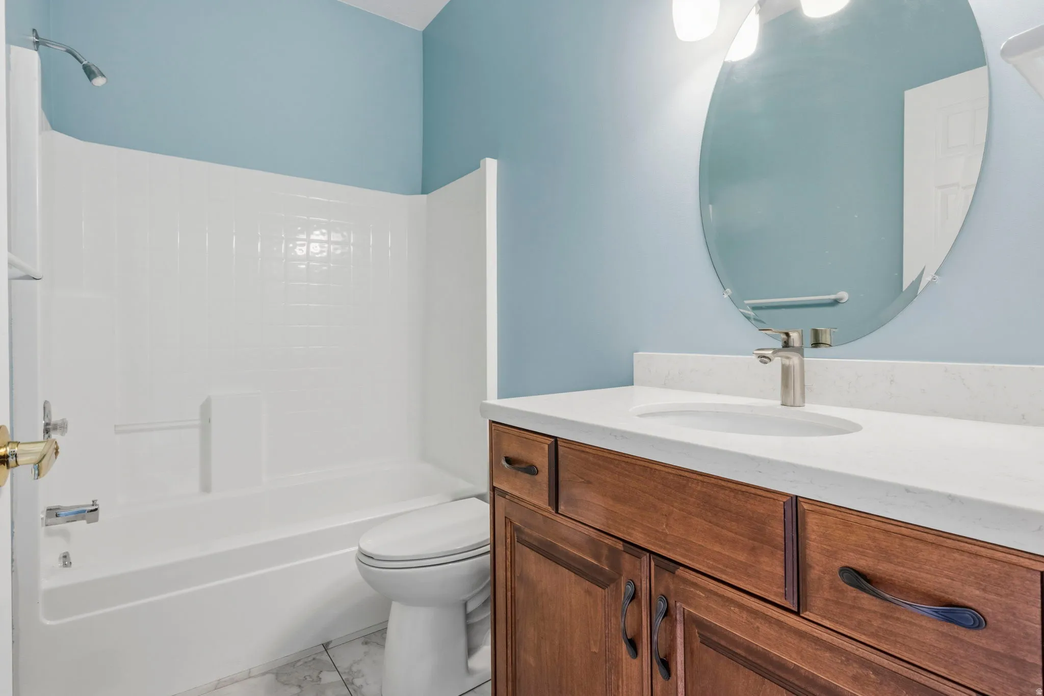 Hall bathroom featuring a wood-finish vanity with a light-toned countertop and an oval mirror