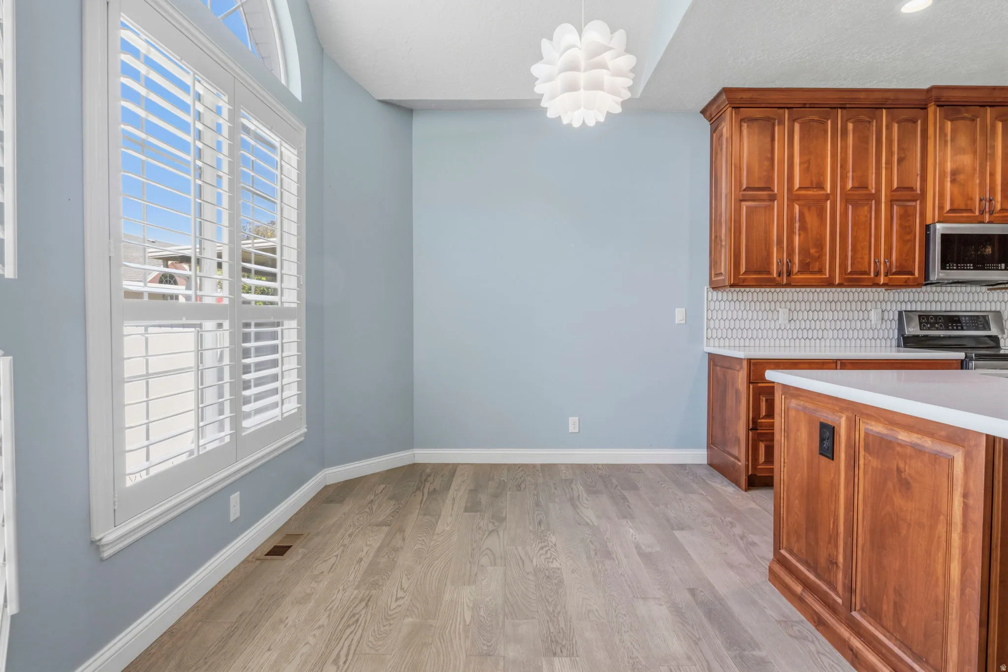 Kitchen and dining area featuring warm wood cabinetry, light-toned wood-finish flooring, and a modern pendant light fixture