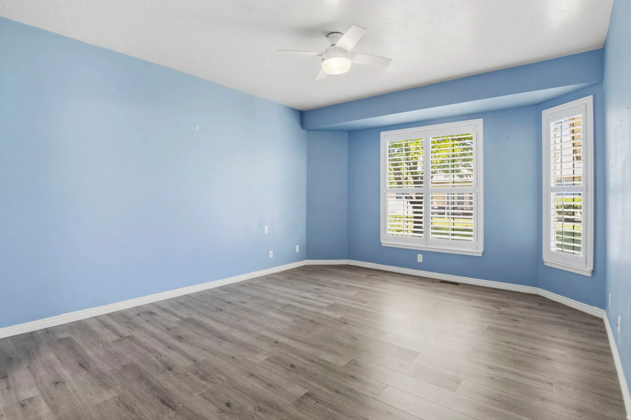 Spacious room featuring wood-finish flooring, a ceiling fan, and white baseboards