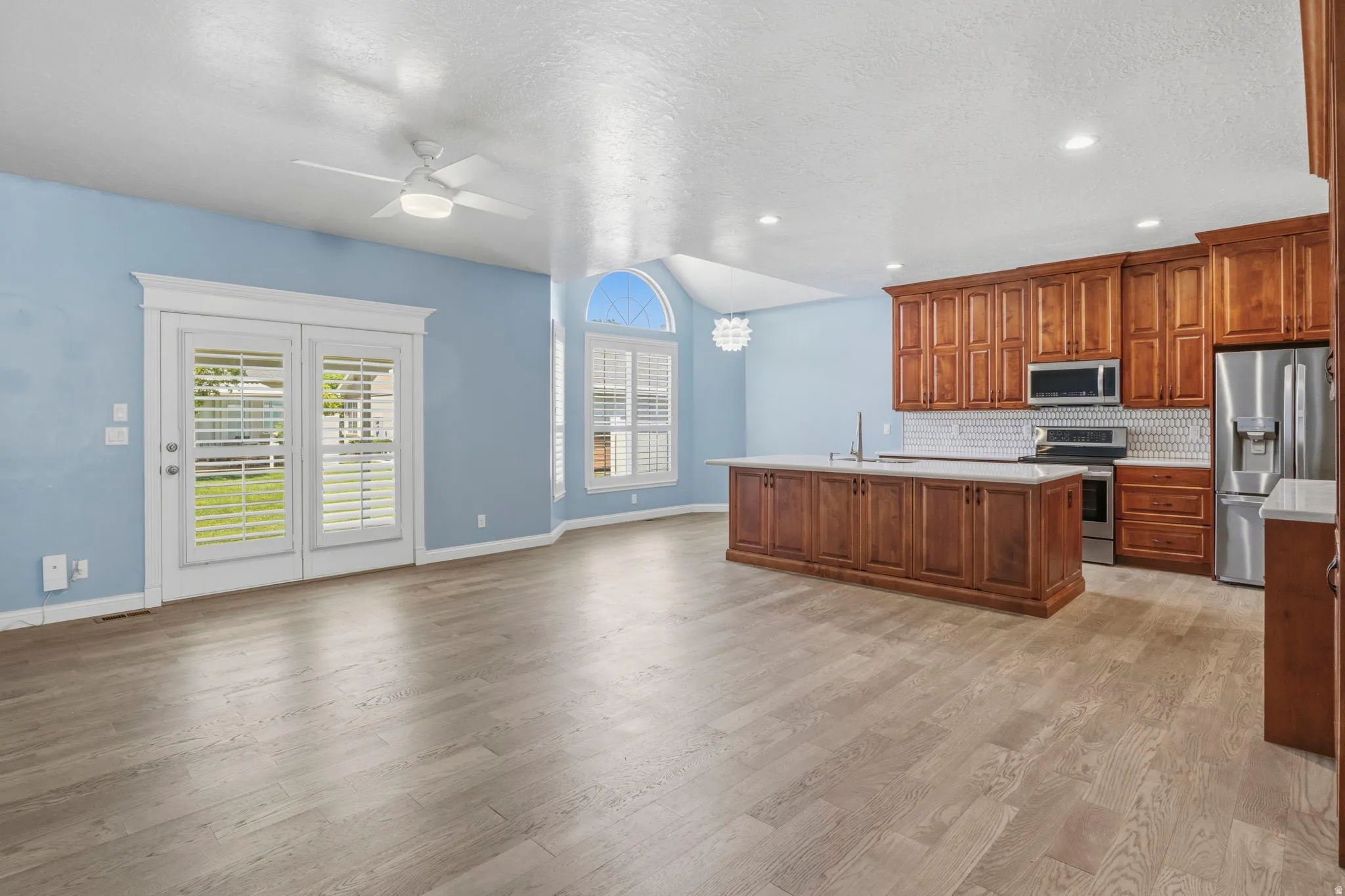 Open-concept living space with wood-finish flooring, vaulted ceilings, and a contemporary ceiling fan