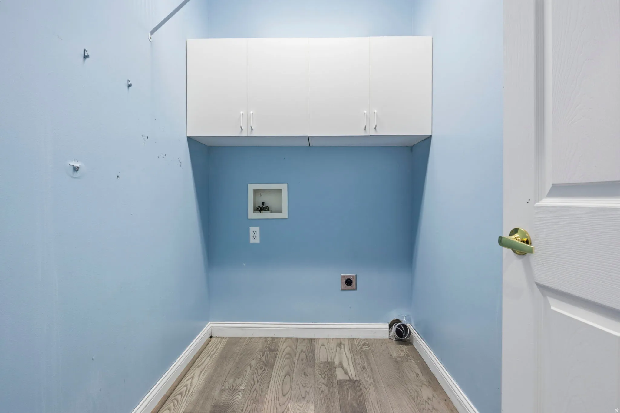 Mainfloor Laundry area featuring upper cabinetry and  wood-finish flooring, baseboards
