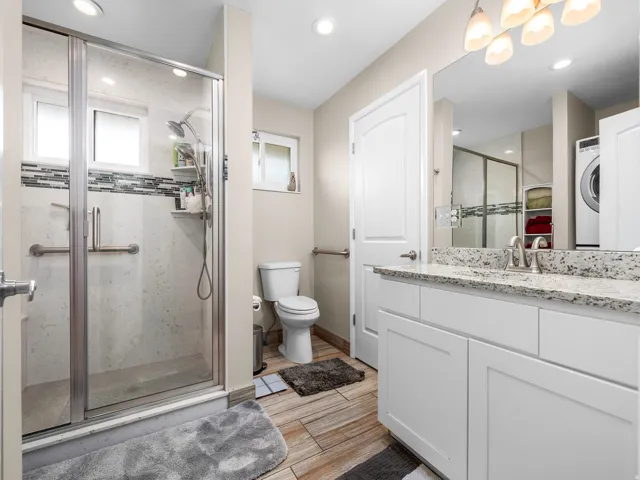 Bathroom featuring a glass-enclosed shower with subway tile surround and mosaic accent, white vanity with stone countertop and integrated sink, recessed lighting, and wood-finish flooring