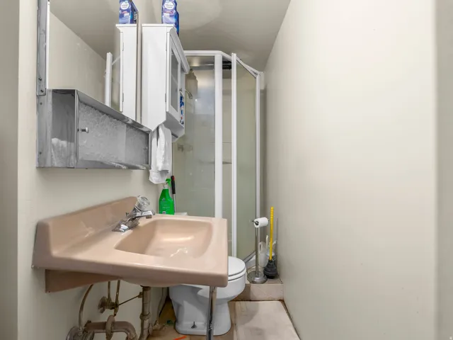 Compact bathroom featuring a corner shower enclosure, a wall-mounted sink with exposed plumbing, and a white medicine cabinet