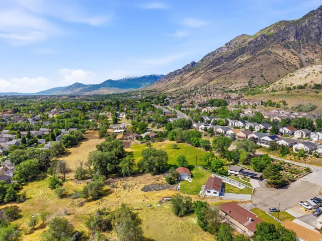 Expansive suburban landscape featuring a mountainous backdrop, scattered residential structures, and mature green trees