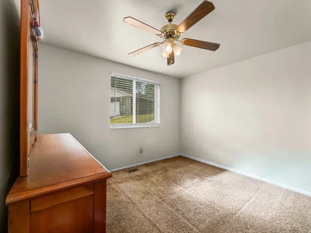 Carpeted room featuring a ceiling fan with integrated lighting, a window with horizontal blinds, and angled ceilings