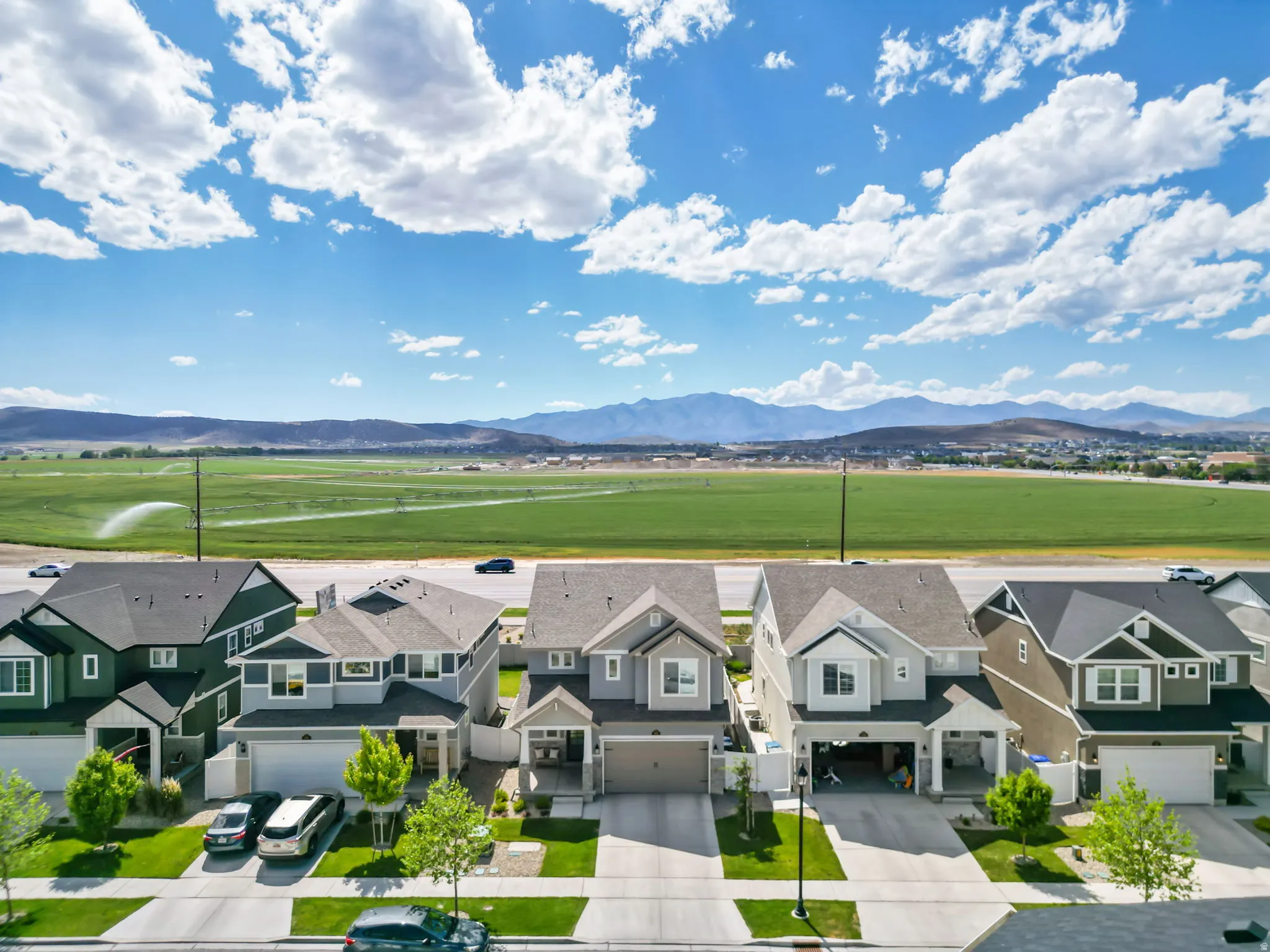 Aerial perspective showcasing multiple properties with mountains and expansive green fields in the background