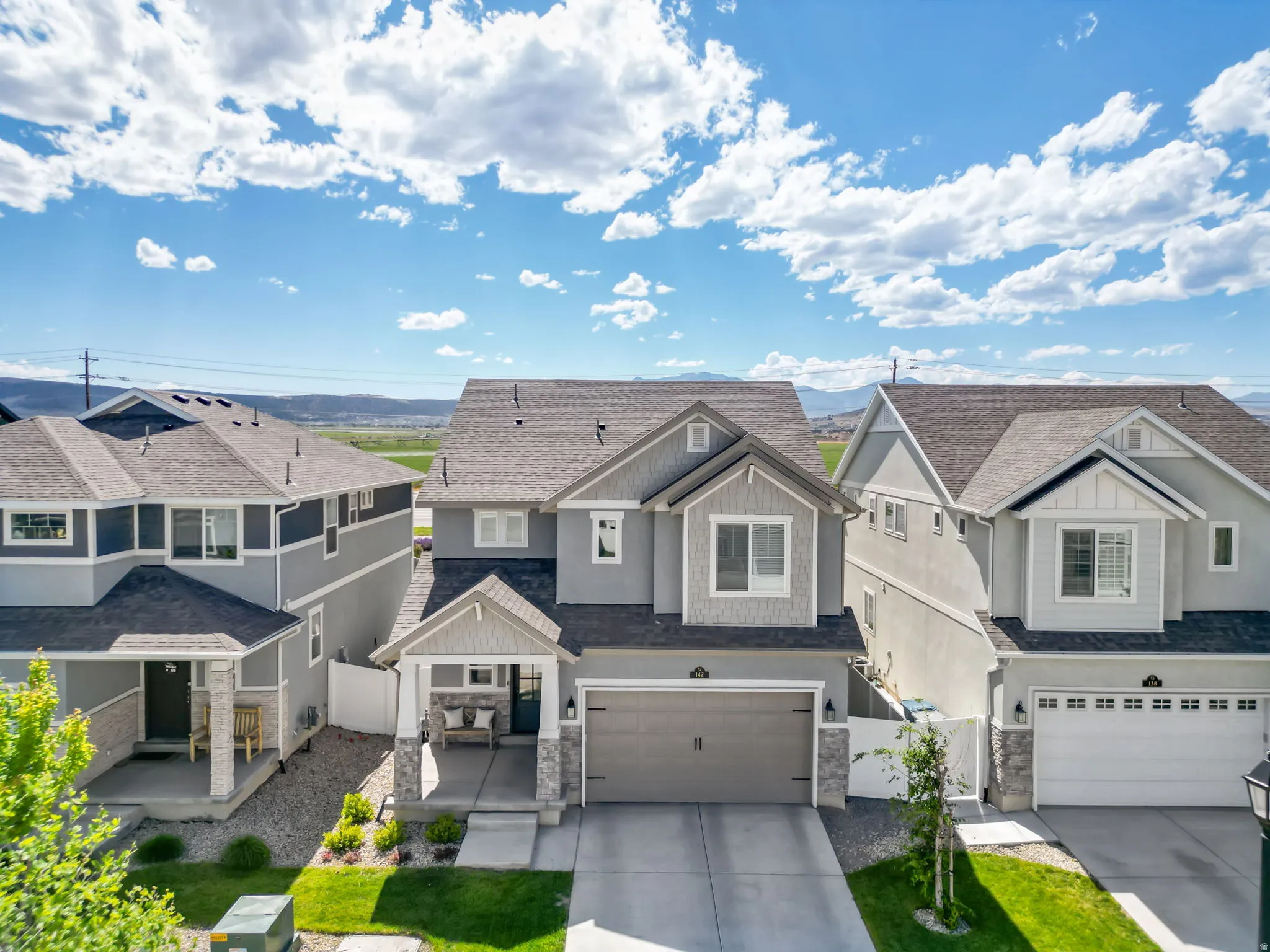 Gray two-story residence featuring a dark asphalt shingle roof, stone accents, and a covered front porch