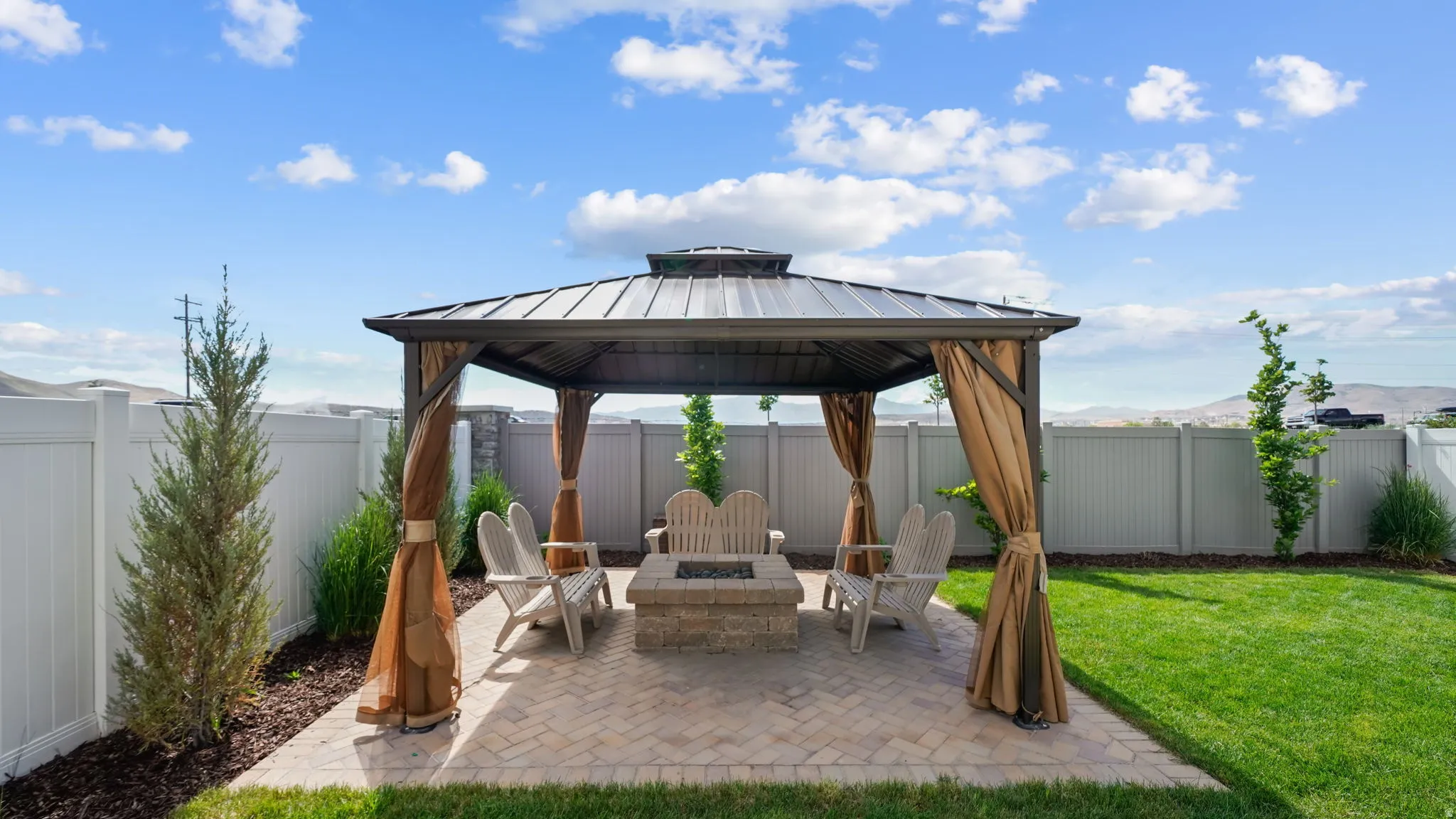 Outdoor patio featuring a covered gazebo with privacy drapes, a built-in fire pit, and paver flooring