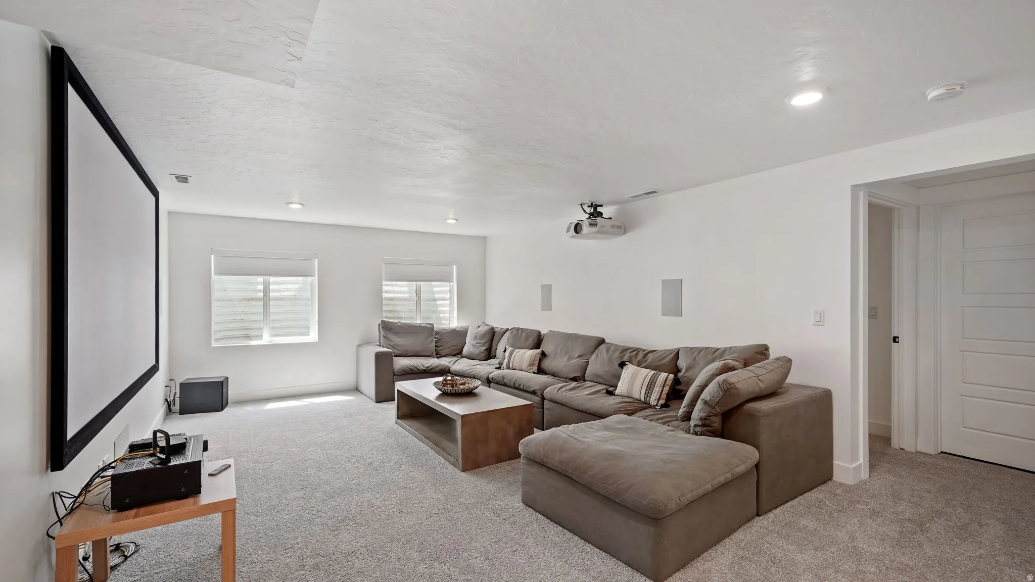 Dedicated media room featuring a large projection screen, ceiling-mounted projector, recessed lighting, and wall-mounted speakers