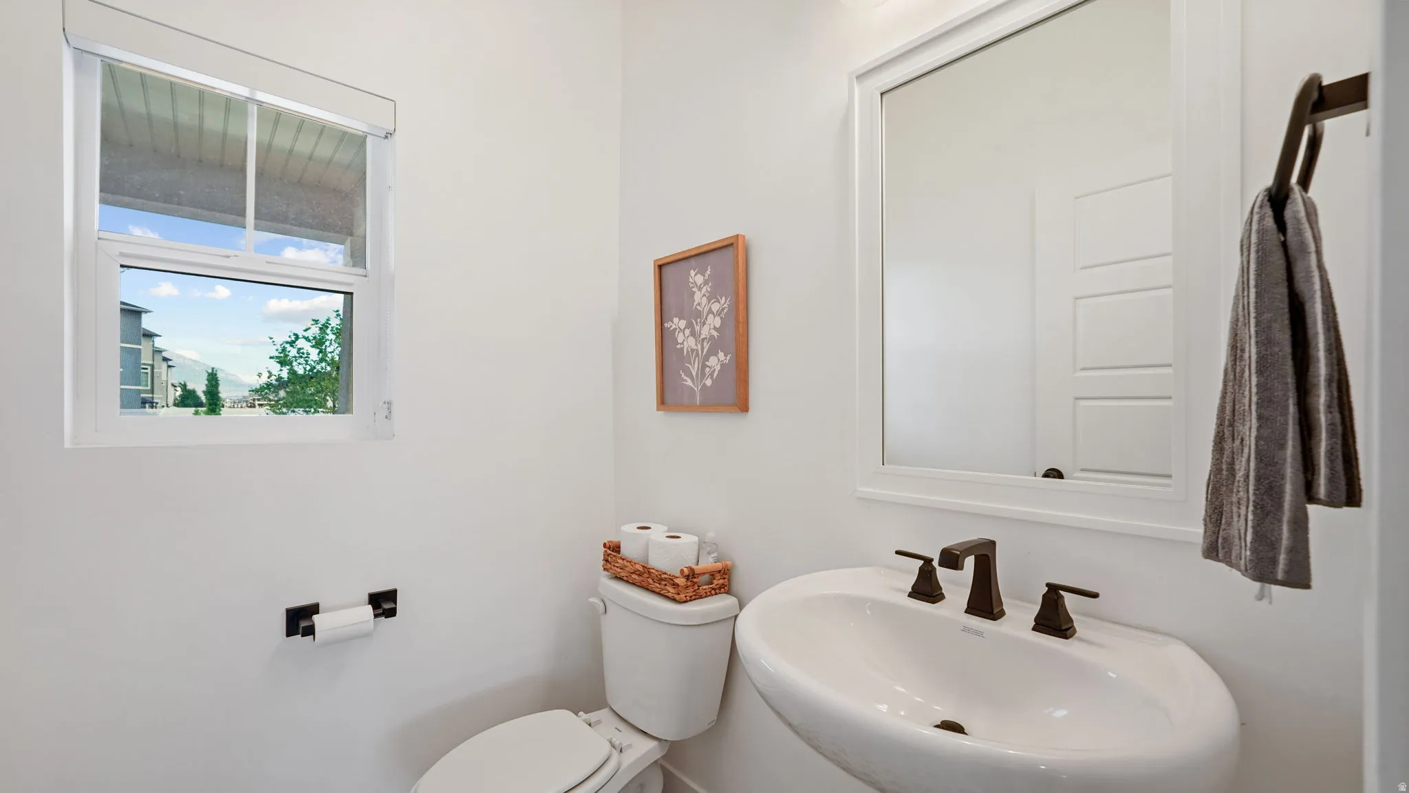 Pedestal sink with dark bronze fixtures, framed mirror, and a window providing natural light