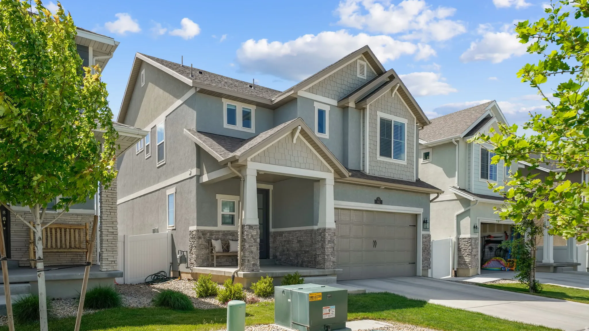 Contemporary two-story residence featuring a front-facing garage, stone veneer accents, covered porch entry, and shingle siding gables