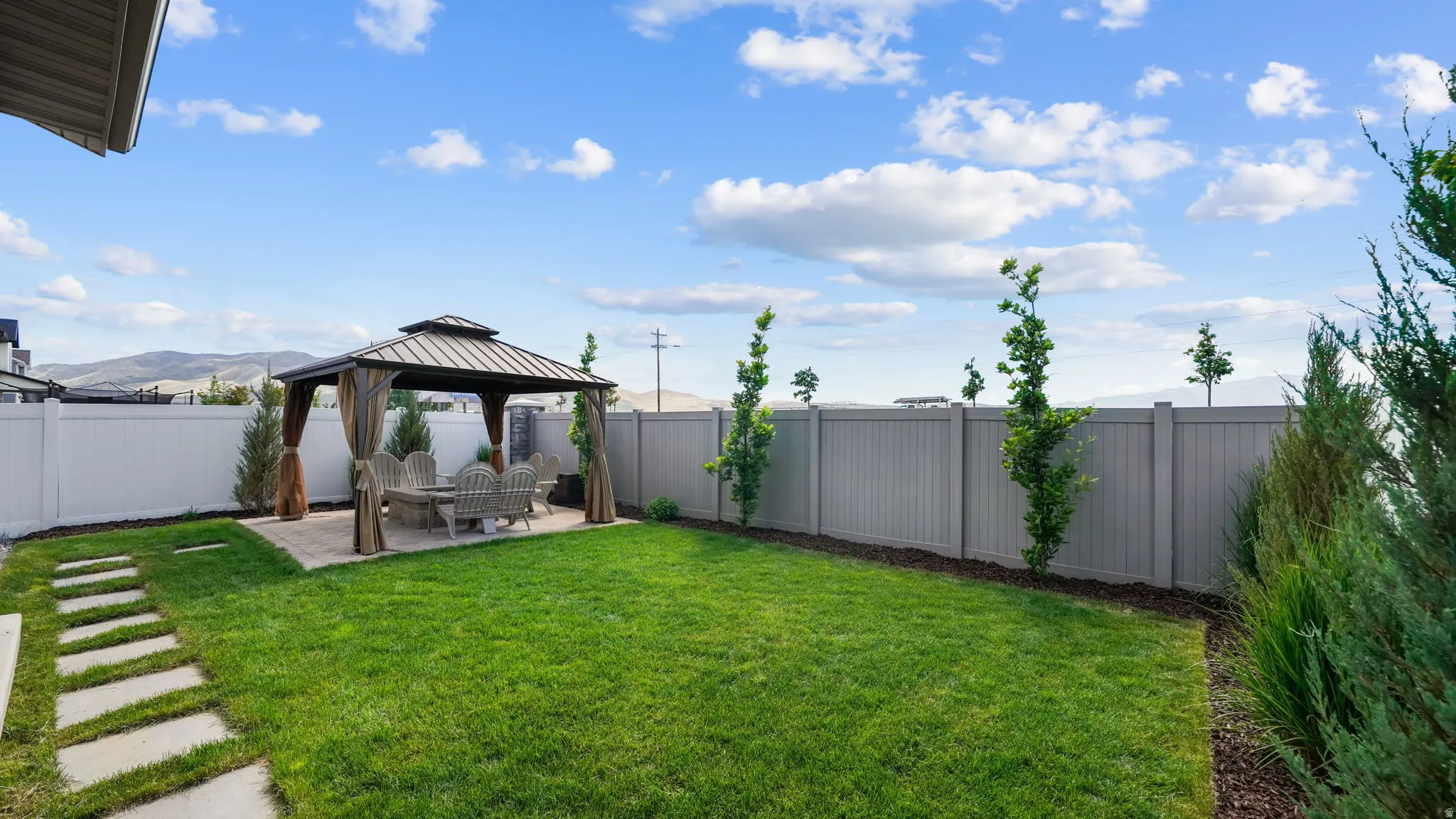 Spacious backyard featuring a central gazebo with privacy drapes, a stone patio, manicured lawn, and a stepping stone pathway