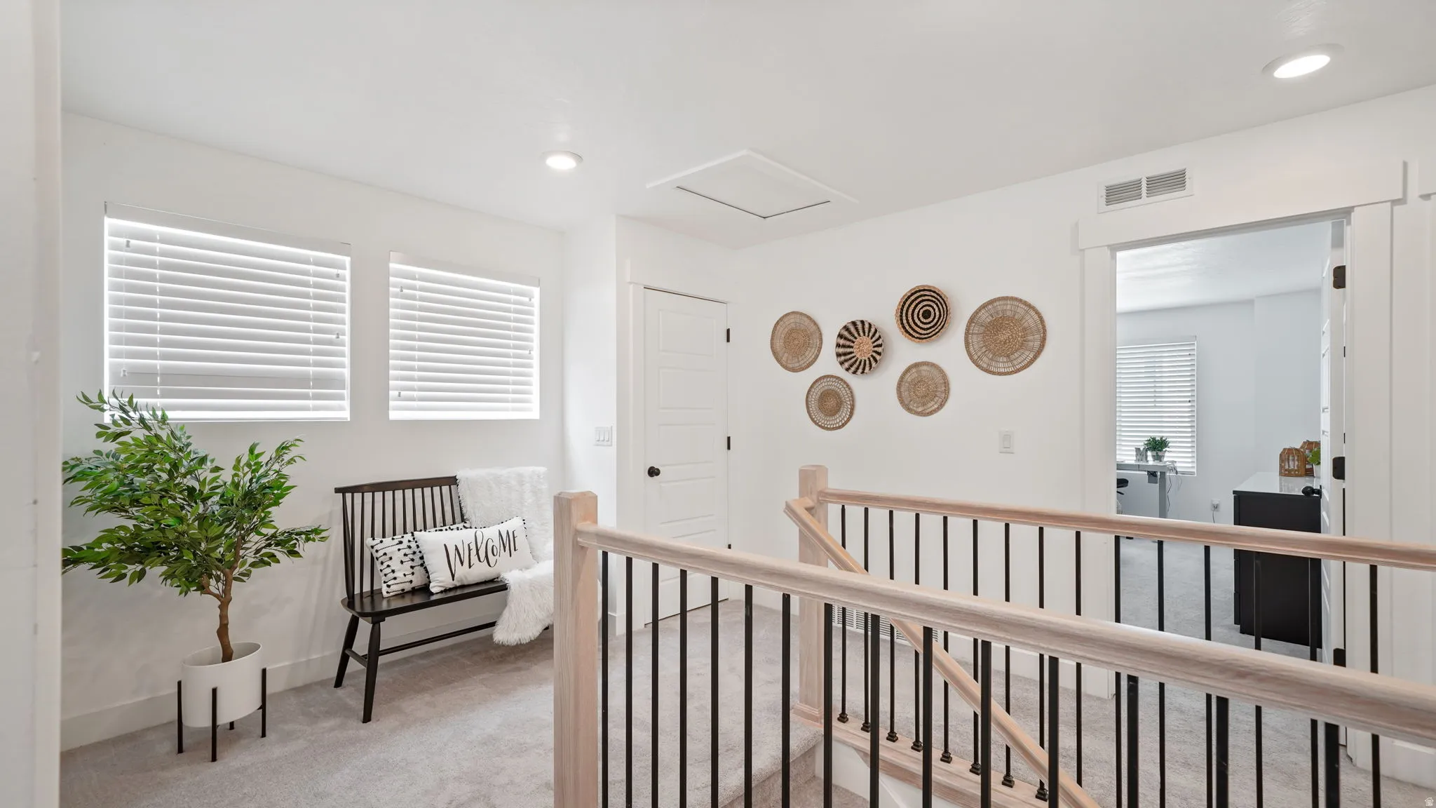Upper-level landing featuring light-toned wood handrails with black metal balusters, recessed lighting, and soft gray carpet