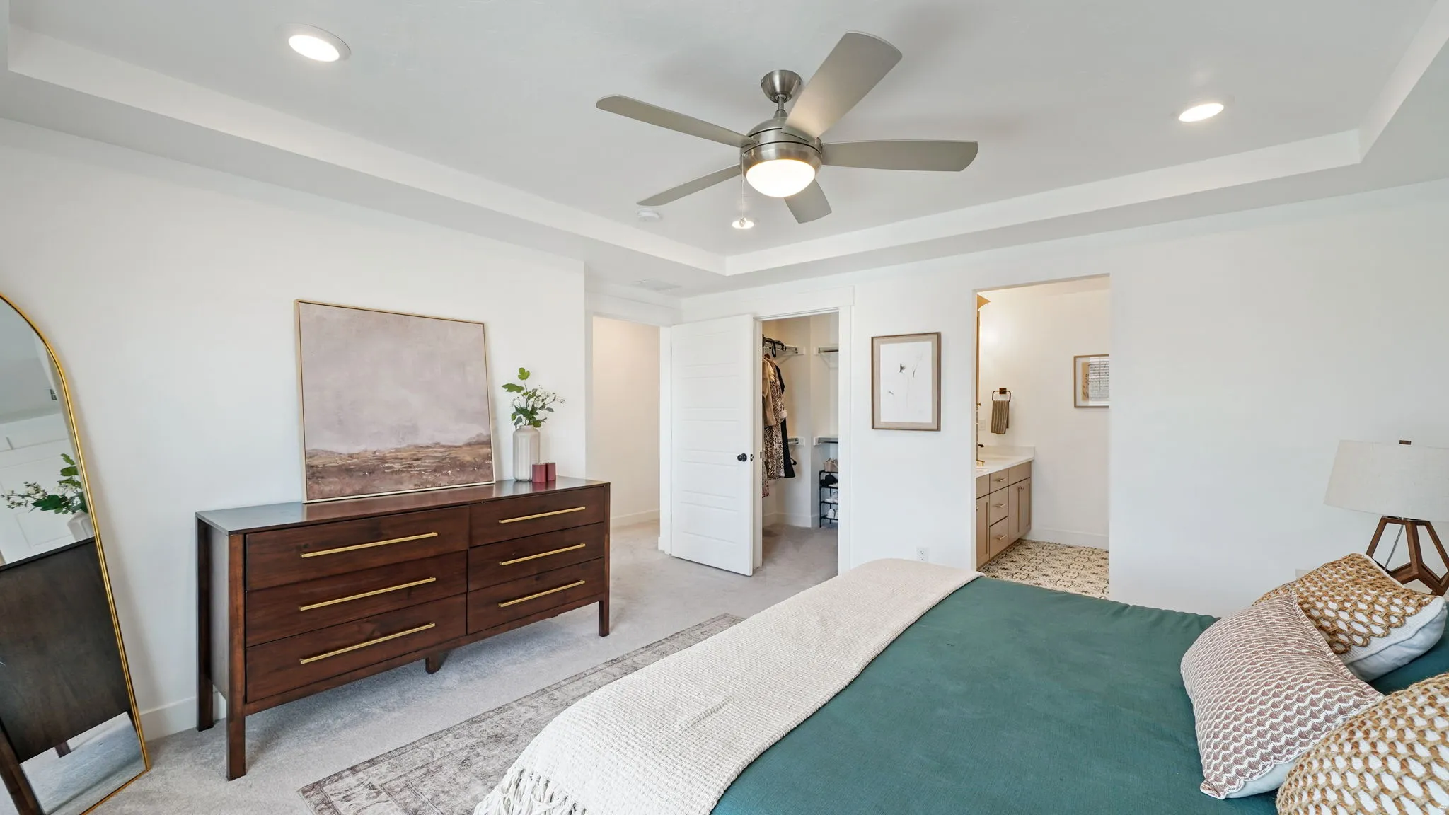 Spacious bedroom featuring light neutral carpeting, a tray ceiling with recessed lighting, and a ceiling fan