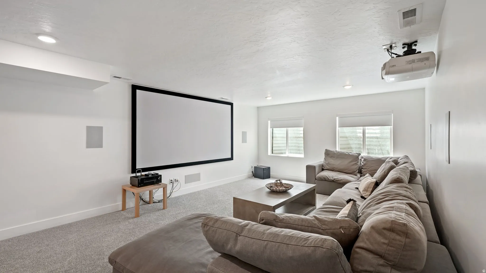 Dedicated media room featuring a large projection screen, mounted projector, recessed lighting, and built-in wall speakers