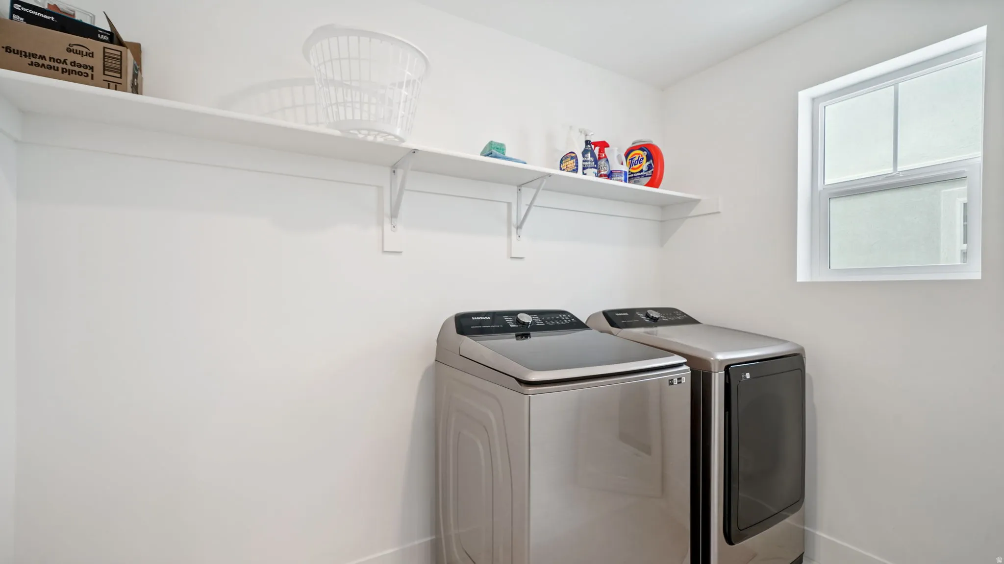 Dedicated laundry space featuring a white wall shelf, a window, and light-colored walls
