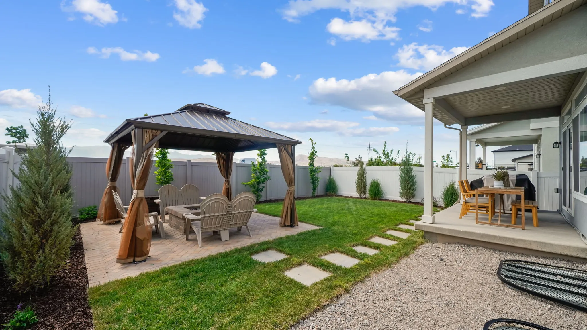 Expansive backyard featuring a covered patio, a separate paved seating area with a gazebo, a manicured lawn, and a low-maintenance gravel section