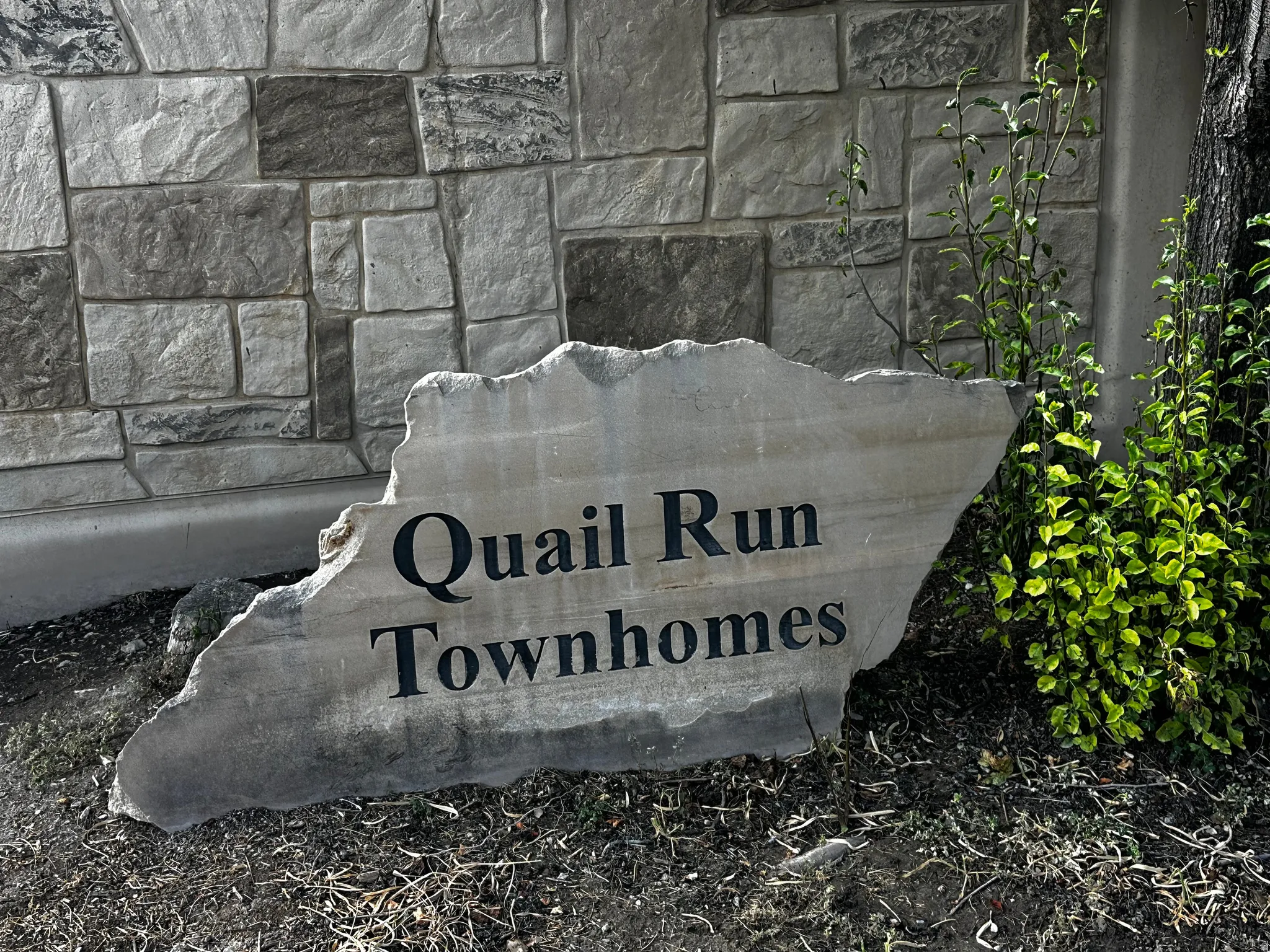 Stone monument sign with "Quail Run Townhomes" inscription, set against a stone facade with varied gray and tan blocks