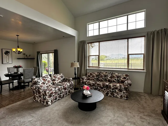 Open-concept living area featuring vaulted ceilings, a large picture window with horizontal blinds, and an upper transom window