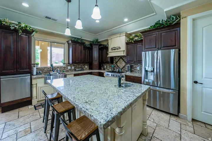 Kitchen featuring a large island with stone countertop, dark wood cabinetry, stainless steel appliances, decorative tiled backsplash, and recessed and pendant lighting