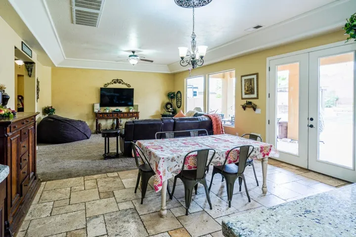 Spacious living area featuring stone-look flooring, carpeted lounge, a decorative chandelier, and double glass-paneled doors opening to the exterior