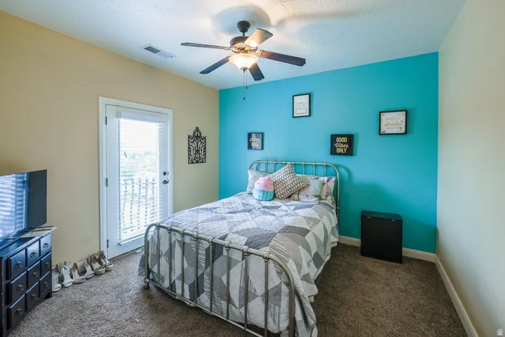Bedroom featuring a ceiling fan, a private balcony access door with integrated blinds, and textured carpeting