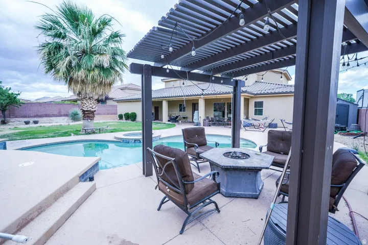 Outdoor living area featuring a custom pergola, integrated fire pit, and a kidney-shaped swimming pool with an attached spa