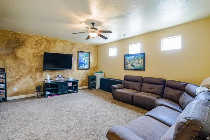 Spacious room featuring textured accent wall, light-colored carpeting, ceiling fan with integrated lighting, and multiple high-set windows