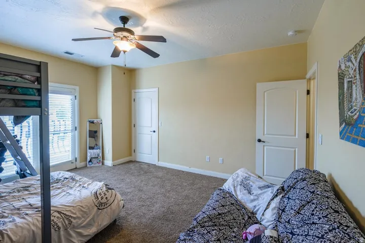 Spacious room featuring carpet flooring, a ceiling fan with integrated lighting, and multiple windows with blinds