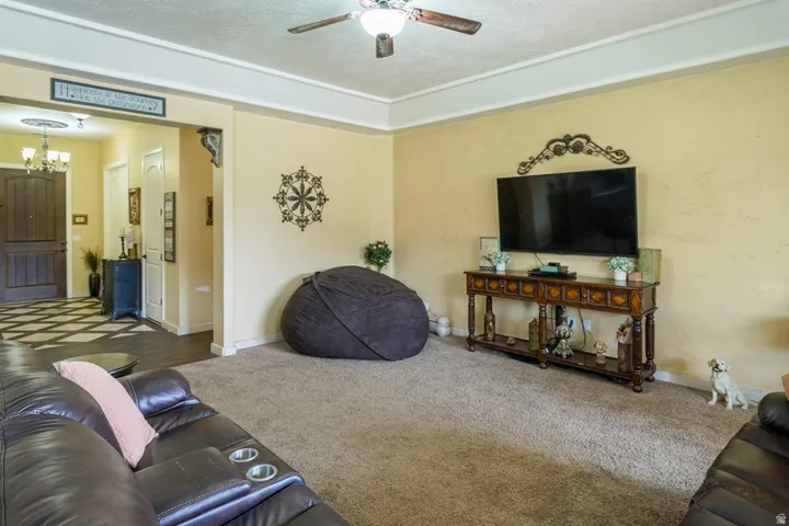 Living area featuring carpet flooring, crown molding, and a ceiling fan with integrated lighting