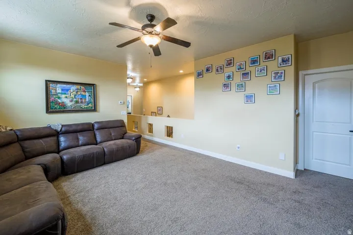 Spacious room featuring textured carpeting, a ceiling fan with integrated lighting, and a white interior door with a black handle