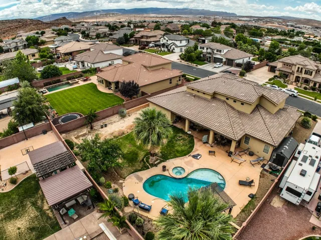 Expansive backyard featuring a large swimming pool with an integrated spa, ample patio space, and mature palm trees