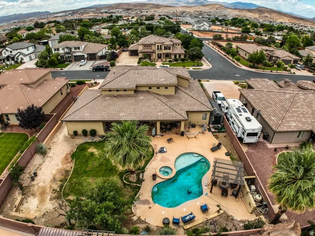 Outdoor living space featuring a freeform swimming pool with integrated spa, an adjacent patio with a pergola, and mature landscaping
