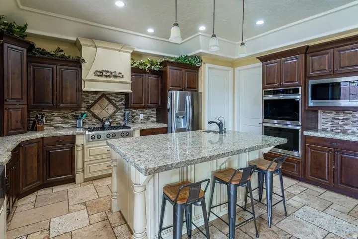 Gourmet kitchen featuring a large central island with seating, granite countertops, stone tile flooring, stainless steel appliances, and rich wood cabinetry