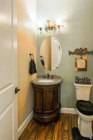Powder room featuring a decorative vanity with a granite countertop, oval undermount sink, and dark wood-finish flooring