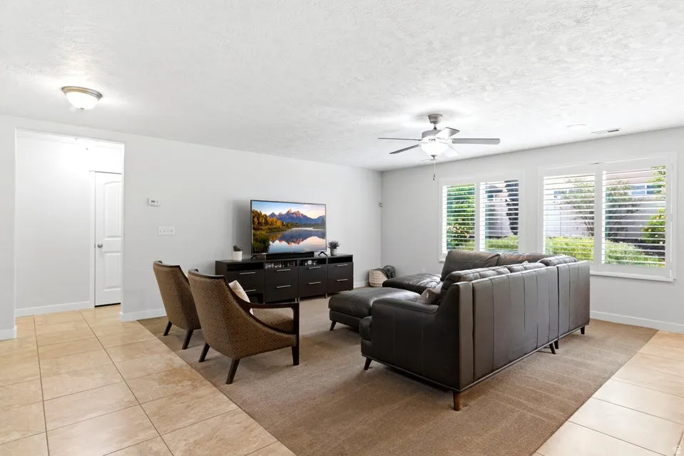 Open concept living space featuring light tan tile flooring, white walls, and multiple windows with white plantation shutters