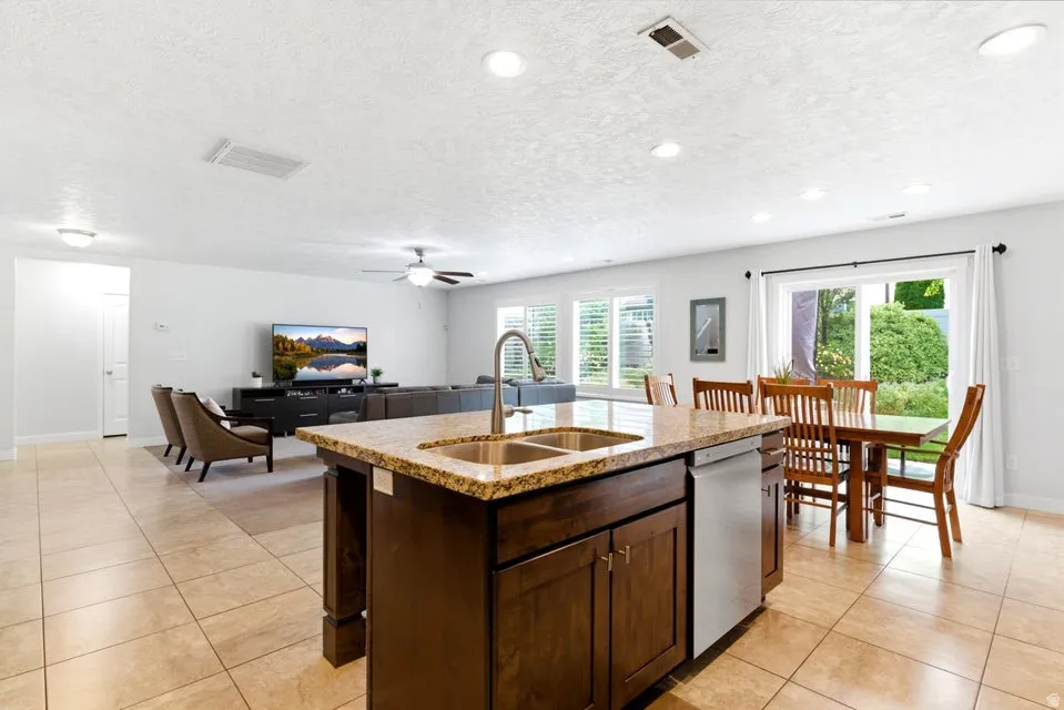 Open-concept living area featuring a kitchen island with granite-finish countertop and double basin sink, stainless steel dishwasher, recessed lighting, and tile flooring