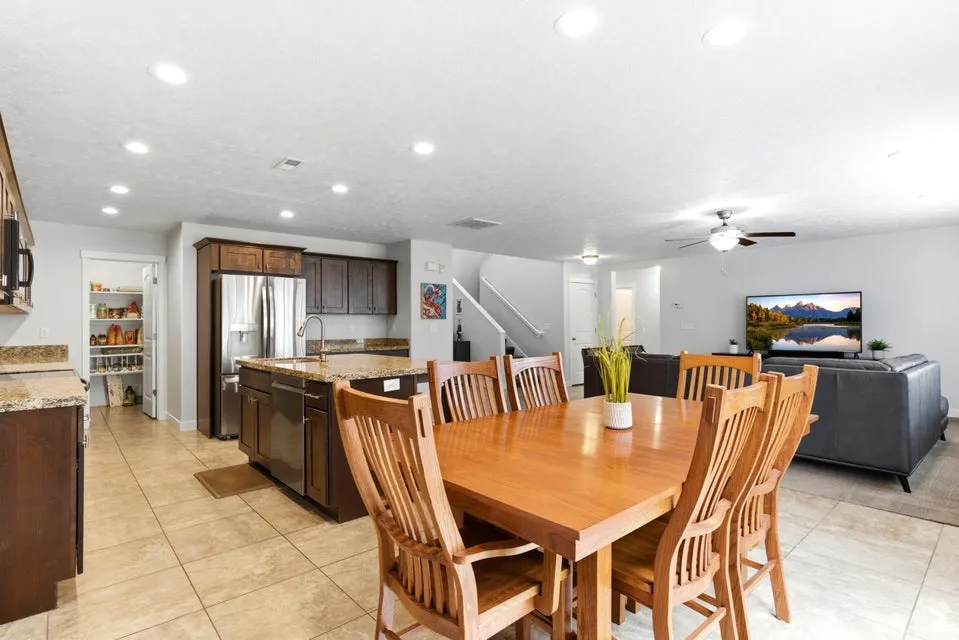 Open-concept interior featuring tile flooring, recessed lighting, a kitchen with dark wood cabinetry, a center island with a sink, and a pantry with built-in shelving