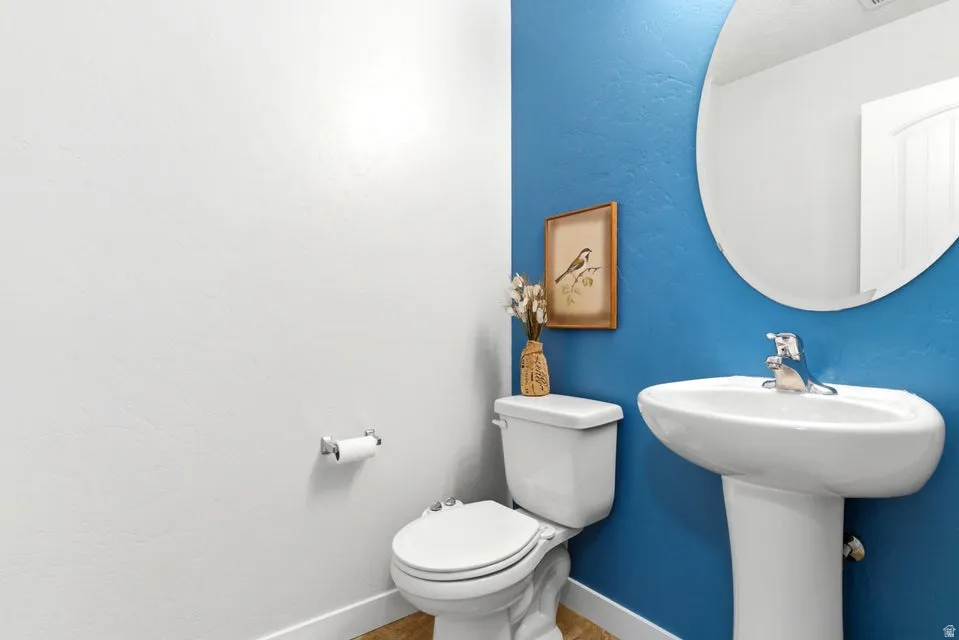 Pedestal sink with a chrome faucet, oval mirror, and a white toilet