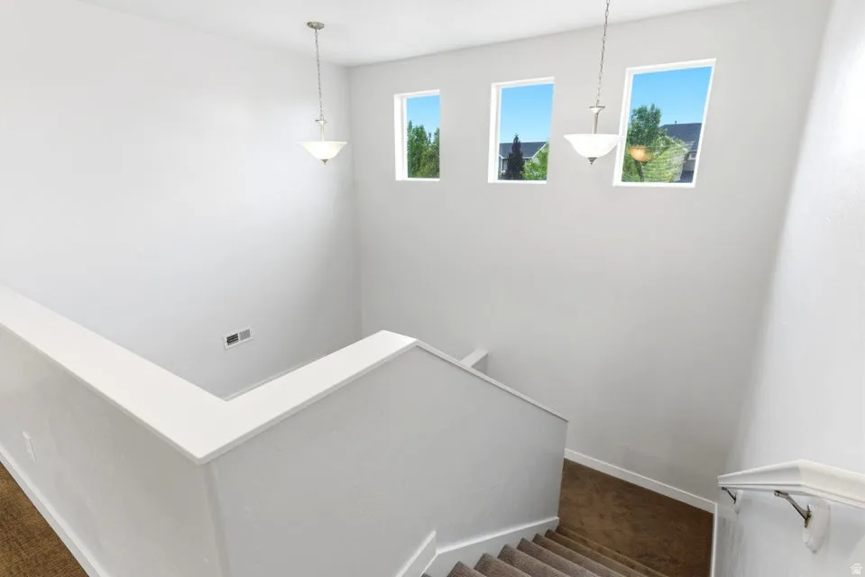 Staircase featuring three rectangular windows, two pendant light fixtures, and carpeted treads