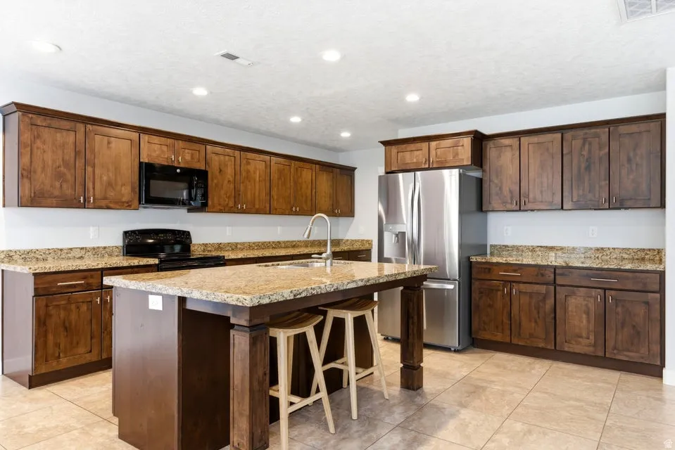 Kitchen featuring a central island with an undermount sink, granite countertops, wood cabinetry, stainless steel refrigerator, and recessed lighting