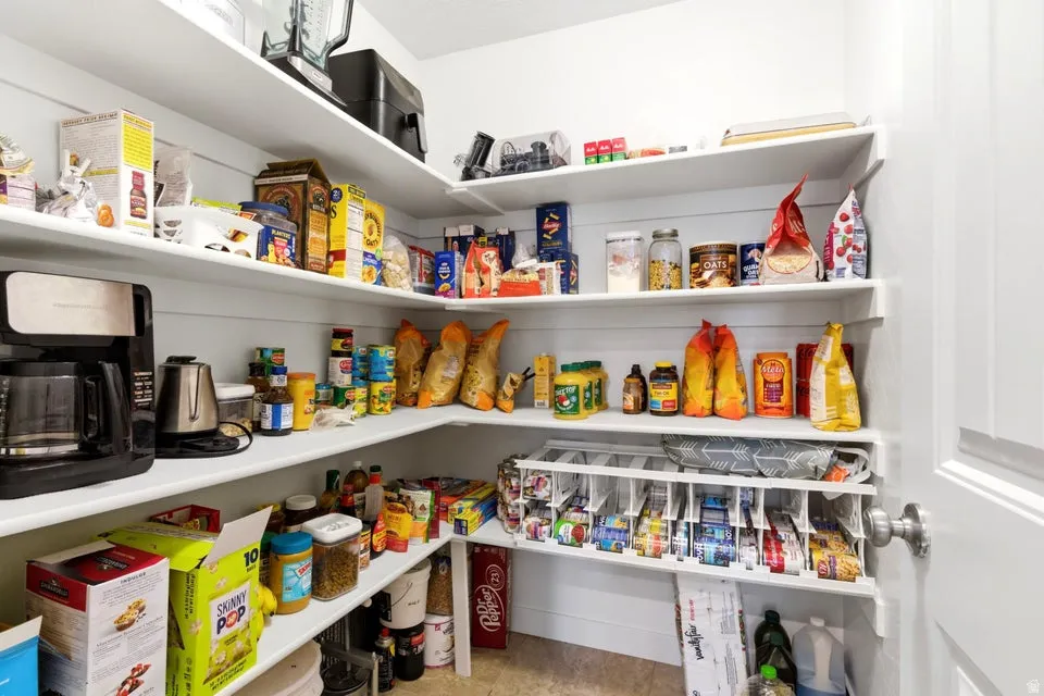 Spacious pantry featuring extensive white shelving, L-shaped configuration, light-colored flooring, and a white paneled door