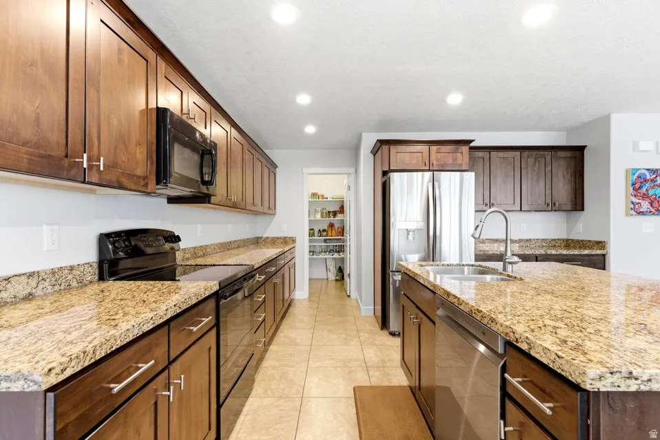 Kitchen featuring extensive cabinetry, stone countertops, stainless steel appliances, a double basin sink, and tile flooring