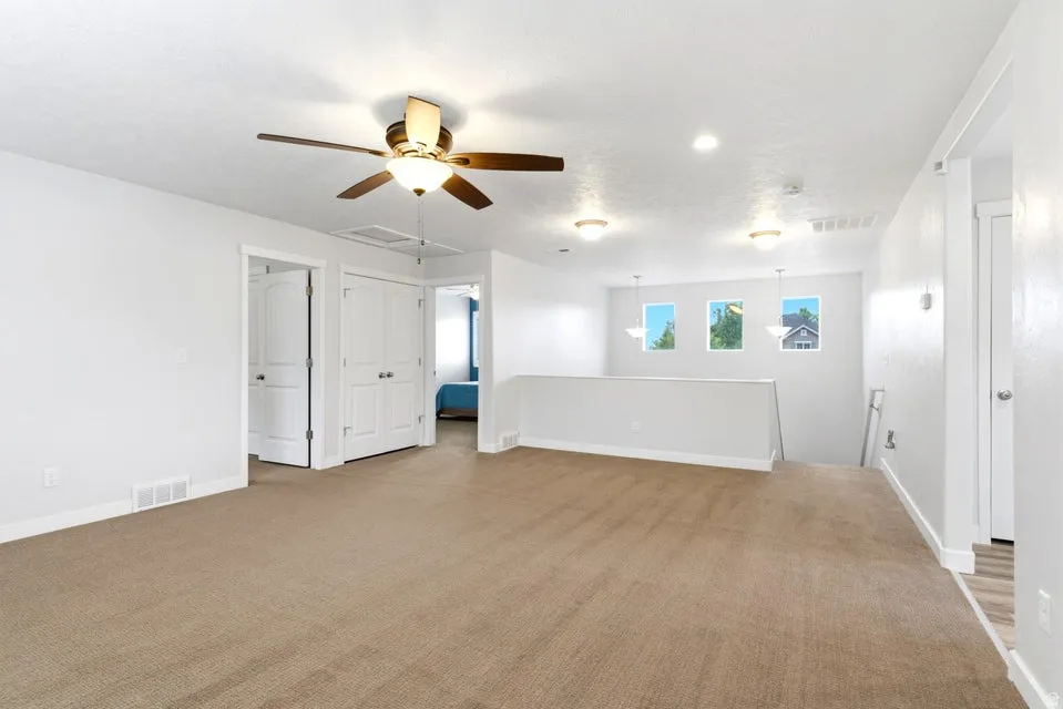 Spacious carpeted area featuring a ceiling fan with integrated lighting, recessed lighting, and three square windows providing exterior views