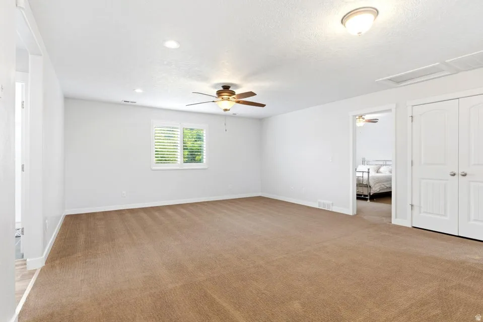 Spacious room featuring neutral carpet flooring, recessed lighting, and a ceiling fan with integrated light
