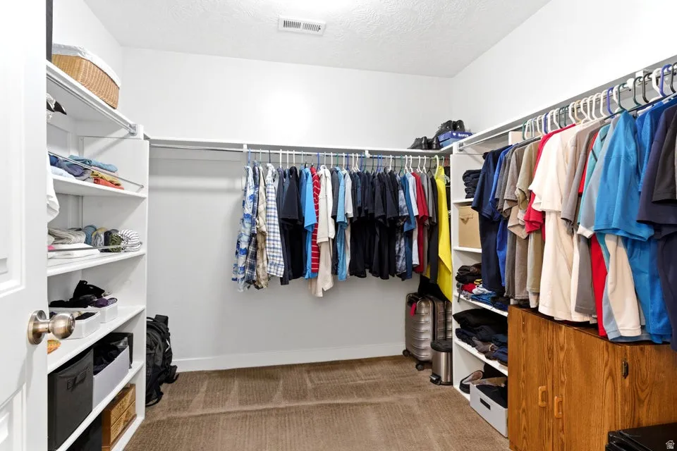 Spacious walk-in closet featuring built-in shelving, multiple hanging rods, and neutral carpet flooring