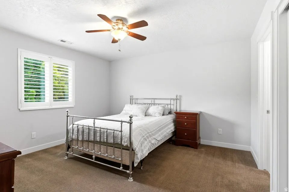 Bedroom featuring a ceiling fan with integrated lighting, window with white plantation shutters, and light-colored walls