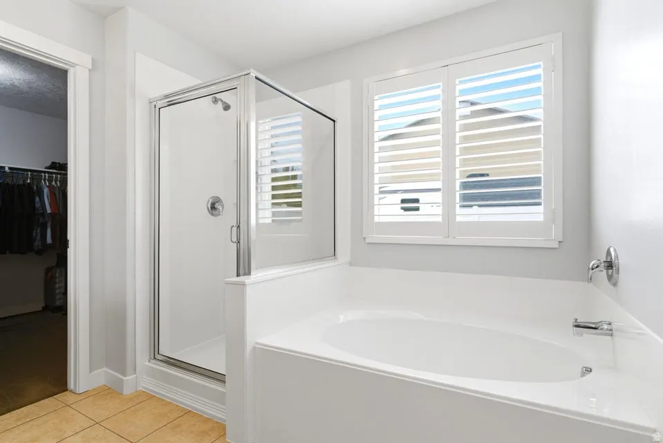 Bathroom featuring a deep soaking tub, separate glass-enclosed shower, white plantation shutters, and ceramic tile flooring