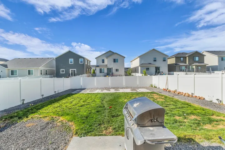 Expansive backyard featuring a lush lawn area, concrete patio space, and white privacy fencing