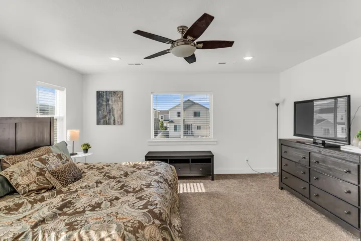 Bright bedroom featuring soft carpet flooring and a ceiling fan with integrated lighting